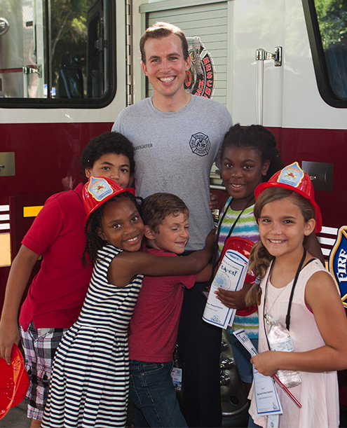 Children hugging a firefighter in front of a fire truck